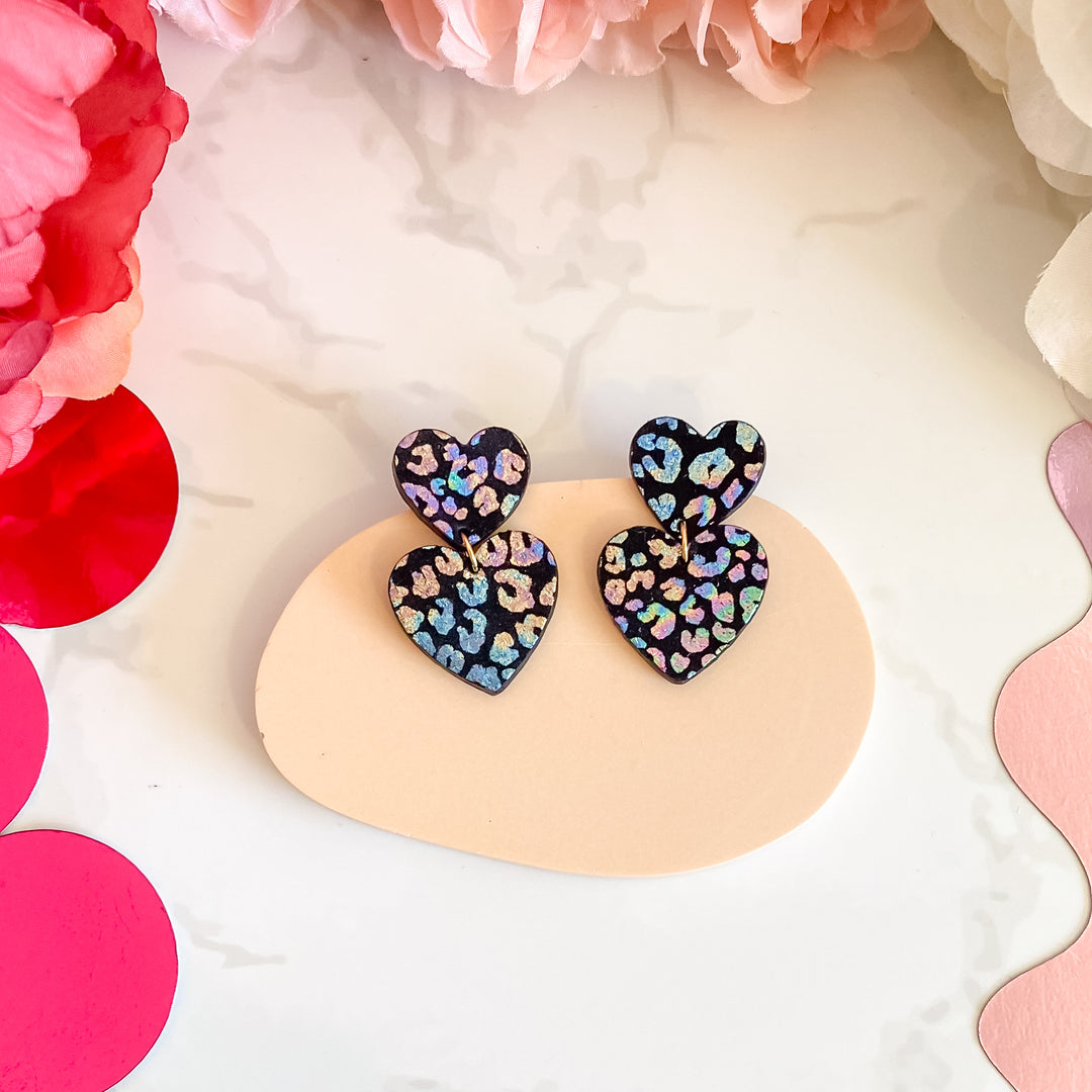 Boucles d’oreilles double cœur en cuir noir leopard holographique, faites main en France par Manali, bijoux artisanaux légers et vibrants.